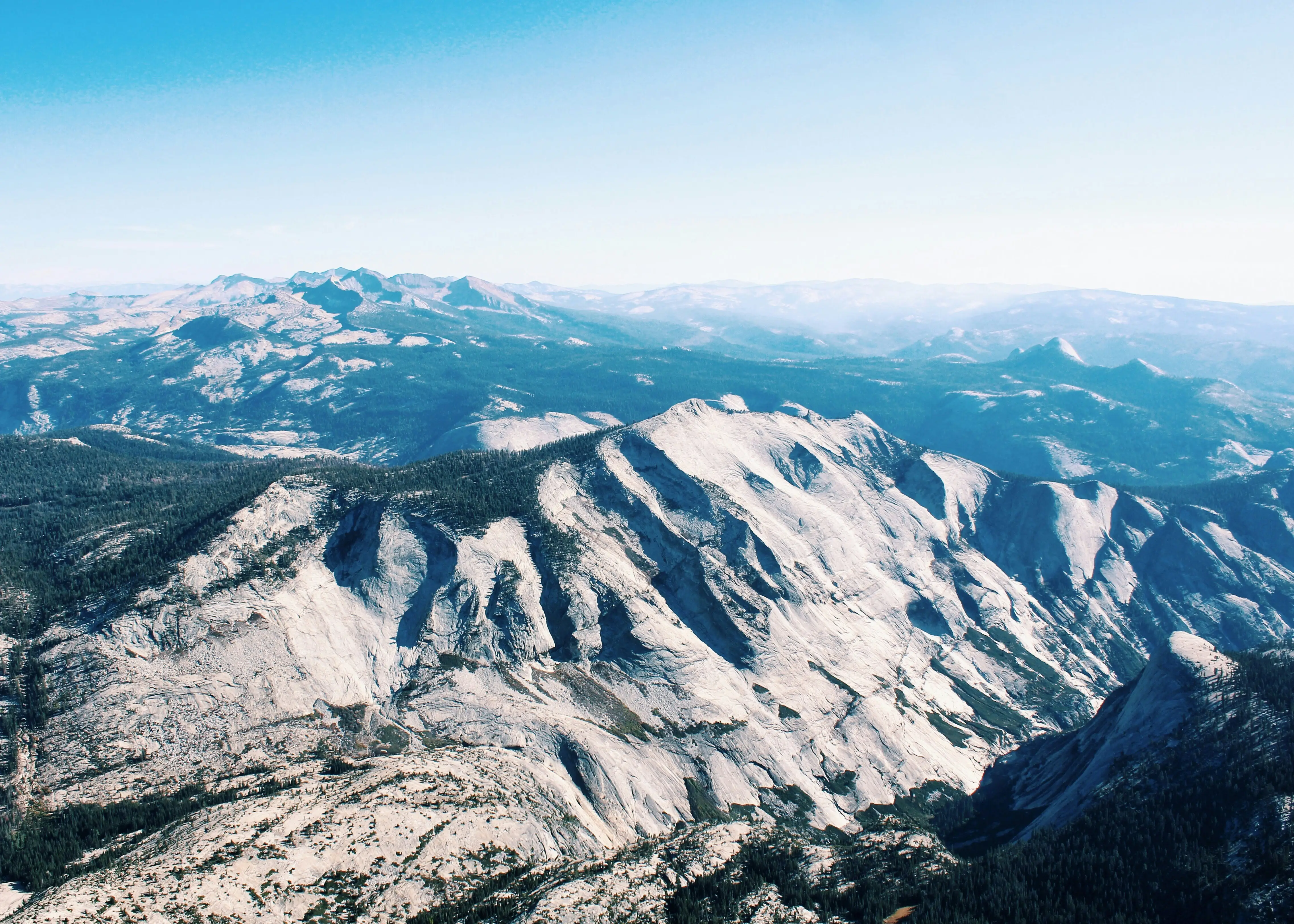 Aerial view of granite mountains and forest under a clear blue sky